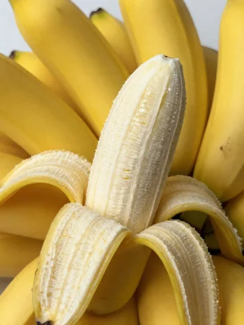 Banana fresca inteira e fatiada, em tigela e mesa rústica